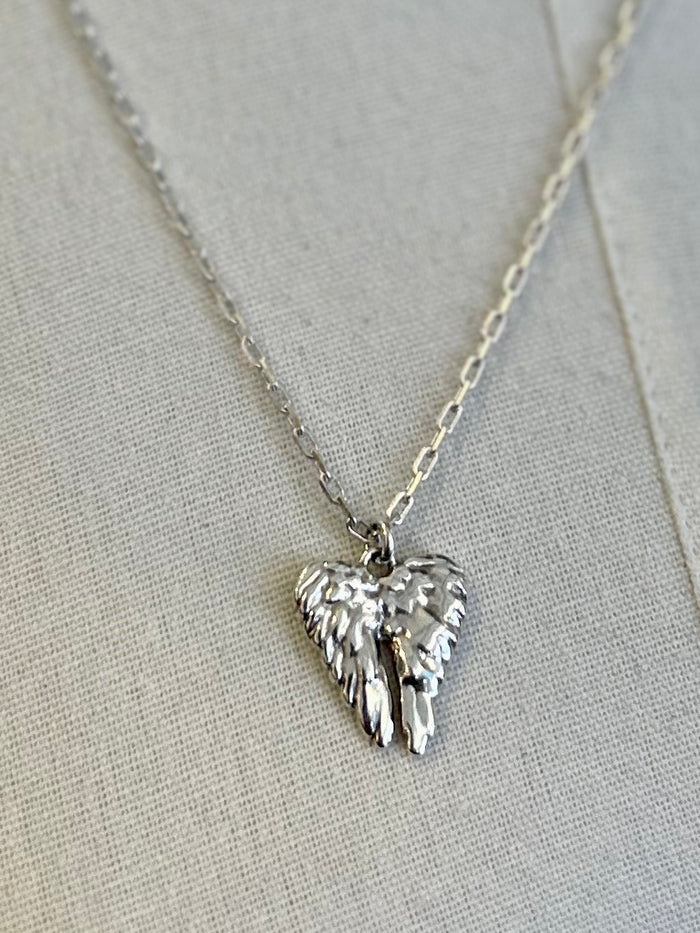Silver heart-shaped pendant with wings on a chain against a light gray background