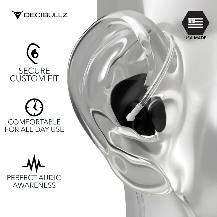 A close-up of a transparent mannequin's ear showing a black Decibullz Custom Moldable Surveillance Radio Headset Earpiece with Awareness inserted. Text on the left reads, “Secure Custom Fit,” “Comfortable for All-Day Use,” and “Perfect Situational Awareness.” Top right features the Decibullz logo and a “USA Made” label with a flag icon.