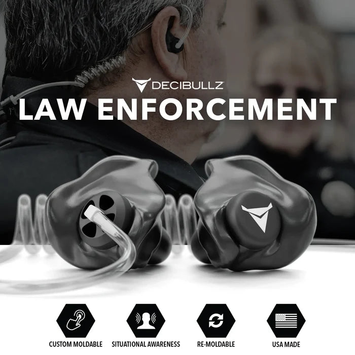 A promotional image for Decibullz Custom Moldable Surveillance Radio Headset Earpieces with Awareness designed for law enforcement. The foreground showcases custom moldable earpieces, featuring icons for custom moldable, situational awareness, re-moldable, and USA made. A blurred person in a police uniform with an acoustic tube radio headset is in the background.