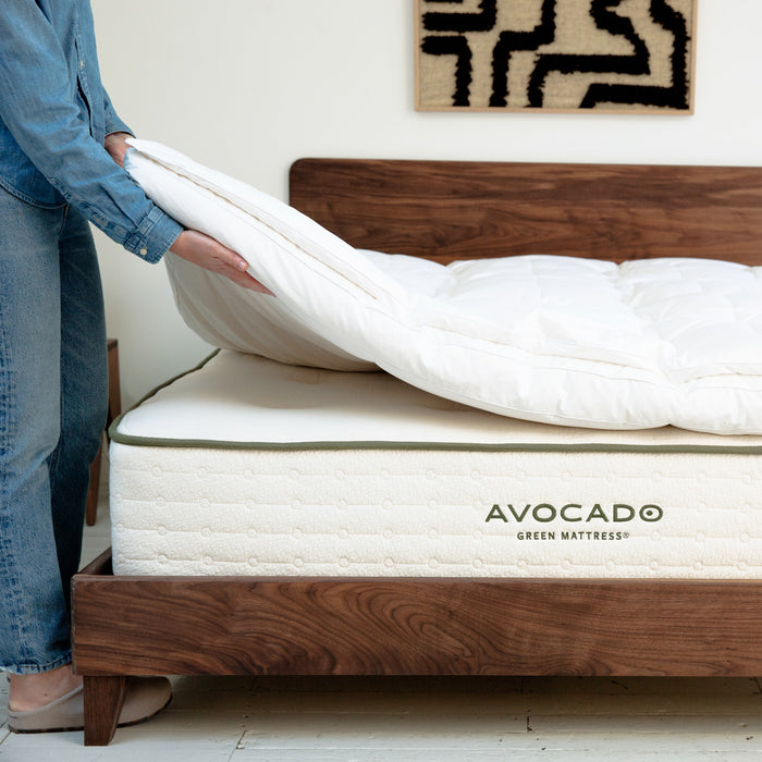 Person adjusting the Down Mattress Topper on an Avocado Green Mattress.