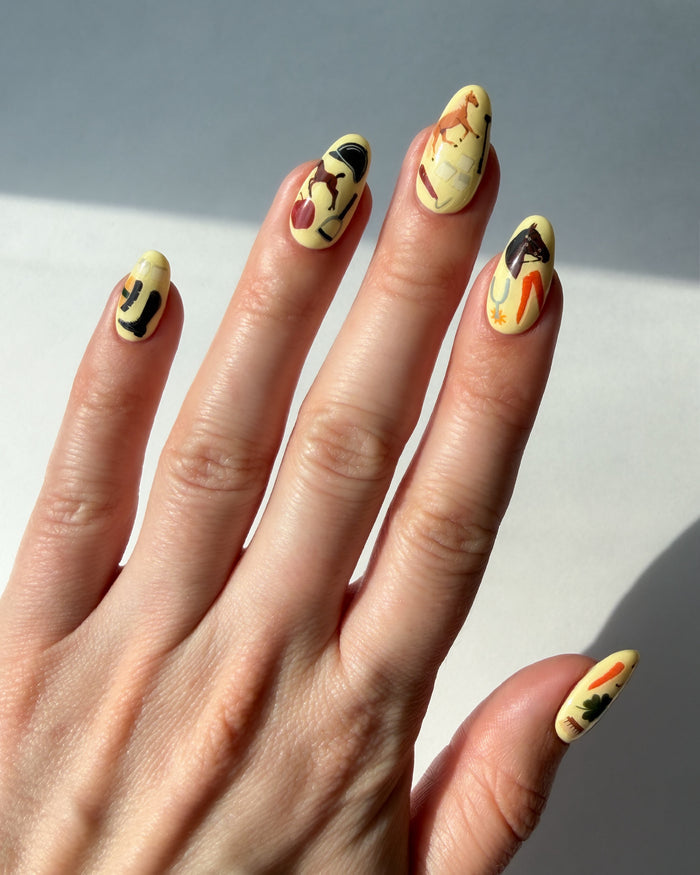 Hand with yellow nail polish and Horse Girl nail art stickers