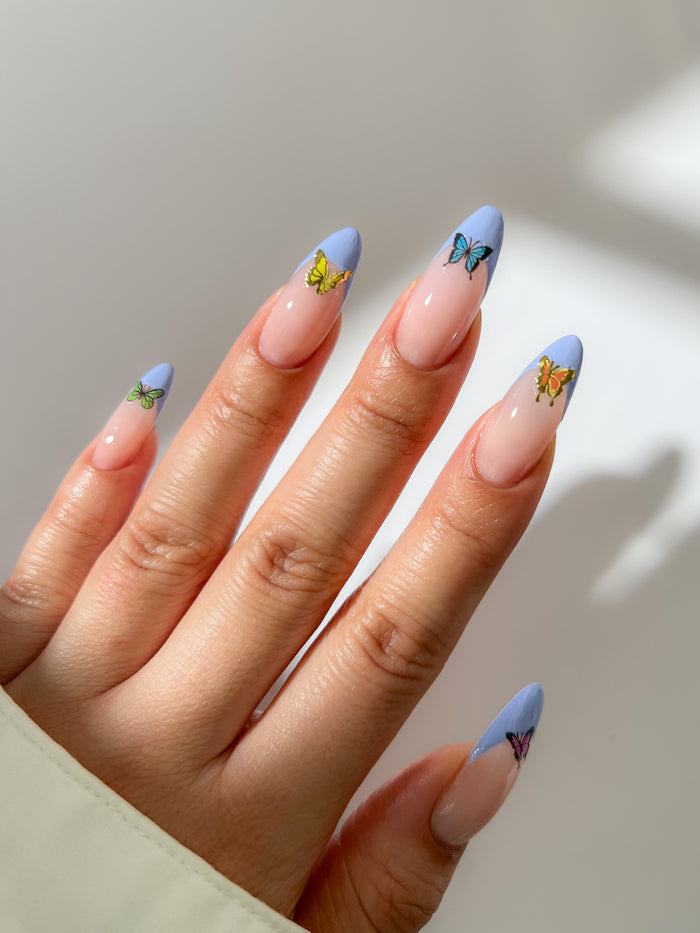 Hand with blue french nails with butterfly stickers on a neutral background