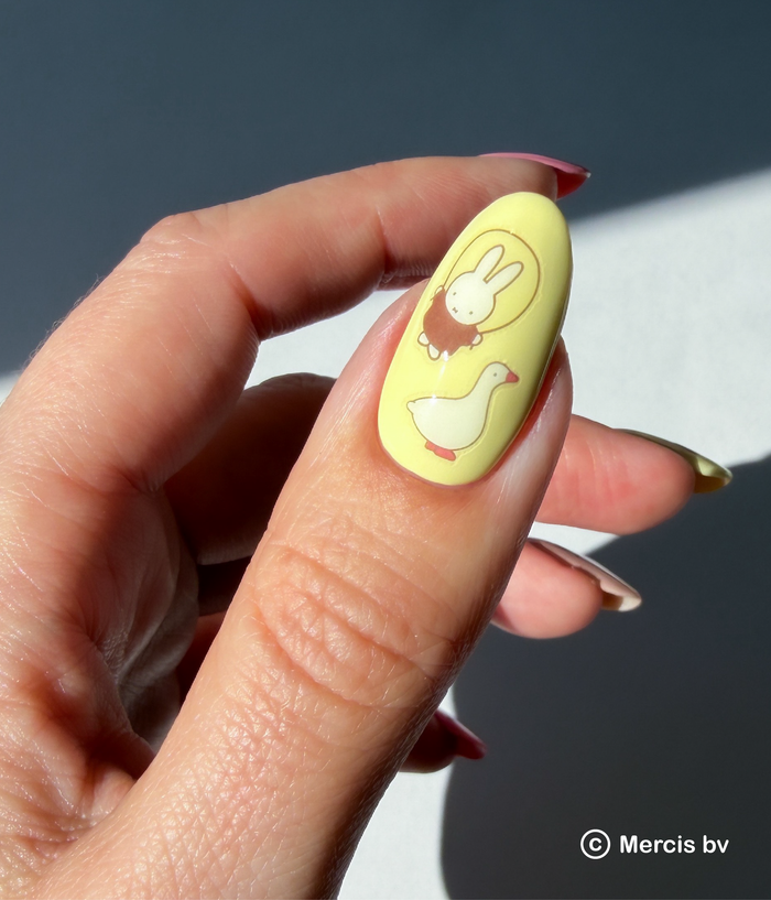Hand with Miffy nail art stickers on a neutral background.