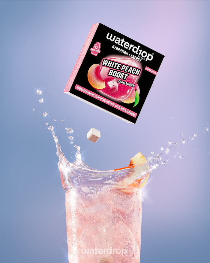 Krabice s nápojem White Peach Boost nad vysokým sklenicí s růžovým nápojem a ledem.