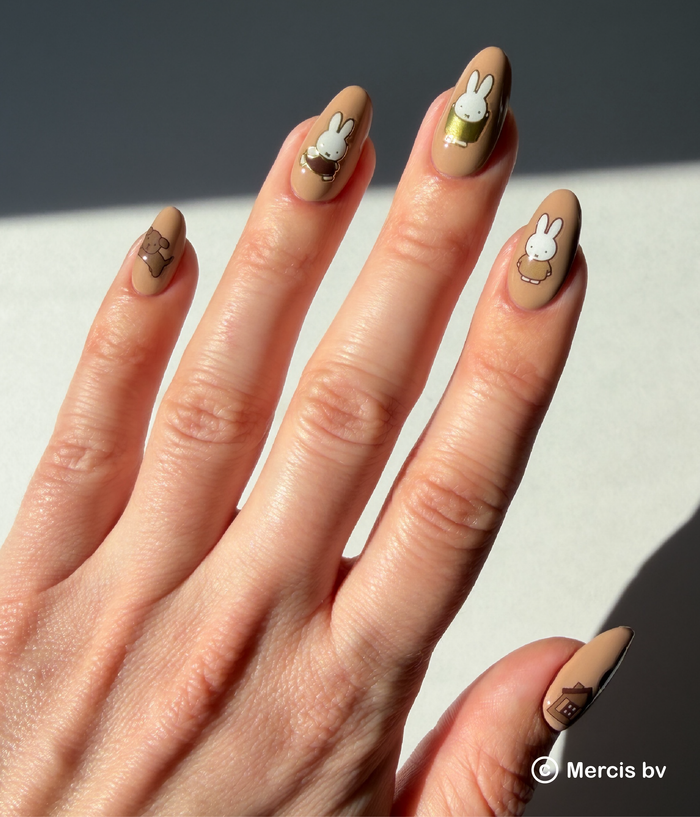 Hand with beige nail polish featuring Miffy designs on a neutral background