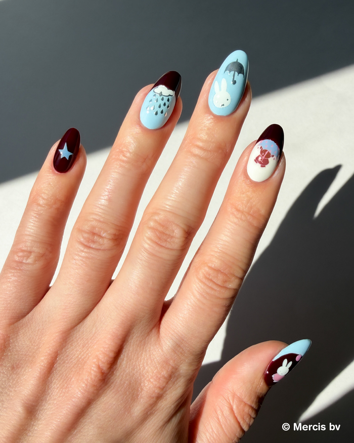 Hand with blue and dark red nails and Miffy stickers on a neutral background.