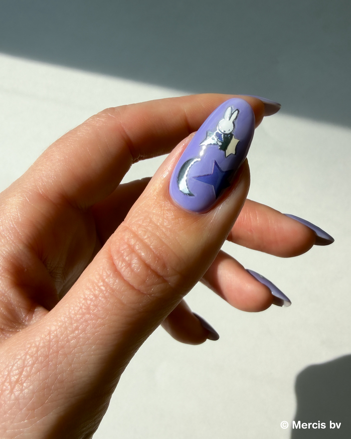 Hand with a purple nail and Miffy stickers on a light background