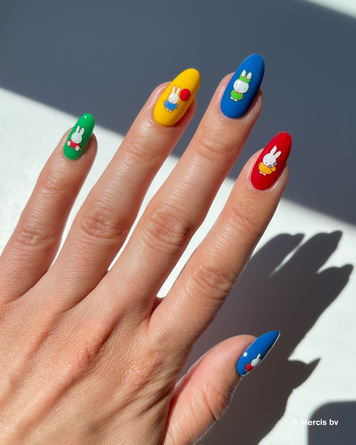 Hand with colorful nail polish and miffy nail art stickers on a neutral background