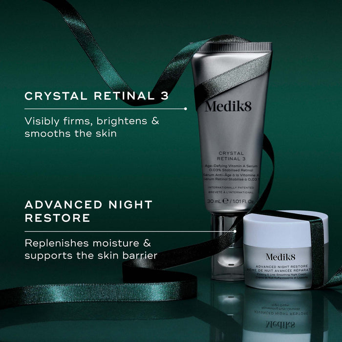 Two Medik8 products wrapped in a green ribbon against a dark green background, with text highlighting key benefits for each. The Crystal Retinal 3 tube "Visibly firms, brightens & smooths the skin," and the Advanced Night Restore travel size jar "Replenishes moisture & supports the skin barrier."