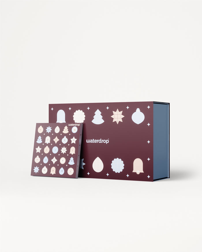 Adventní kalendář s fialovými panely a bílými vánočními ozdobami, zobrazený s modrým vnitřním boxem.