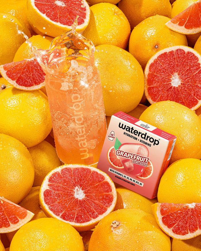 Směs grapefruitů s lahví růžového nápoje grapefruitové příchutě a malou krabičkou mezi ovocem.