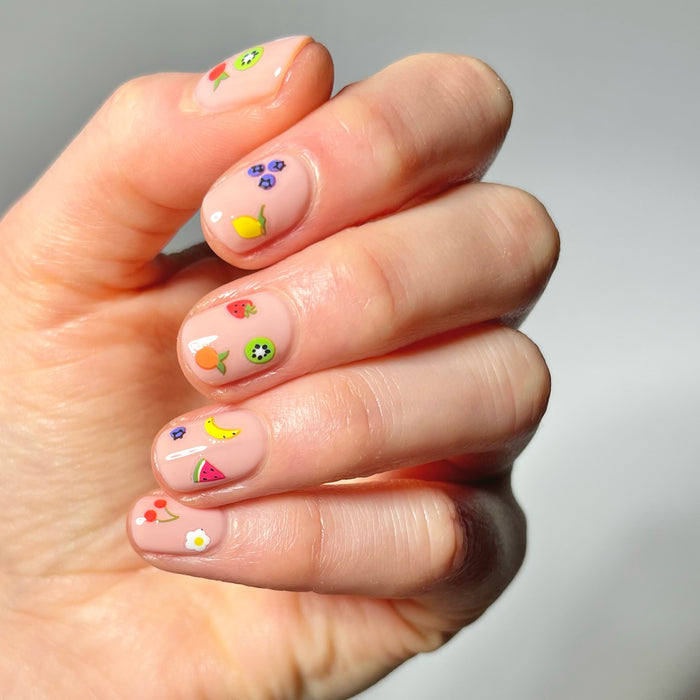 Hand with neutral nail polish and tiny fruit stickers