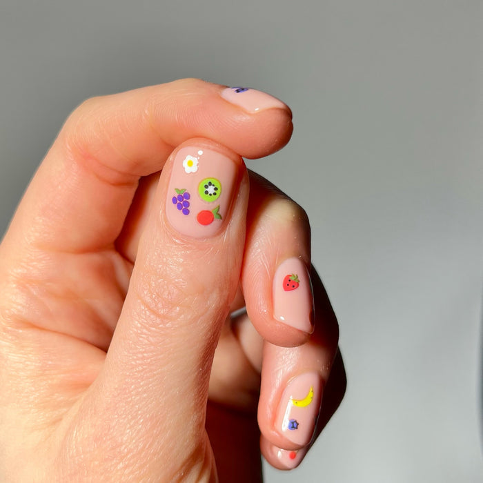 Hand with neutral nail polish and tiny fruit stickers