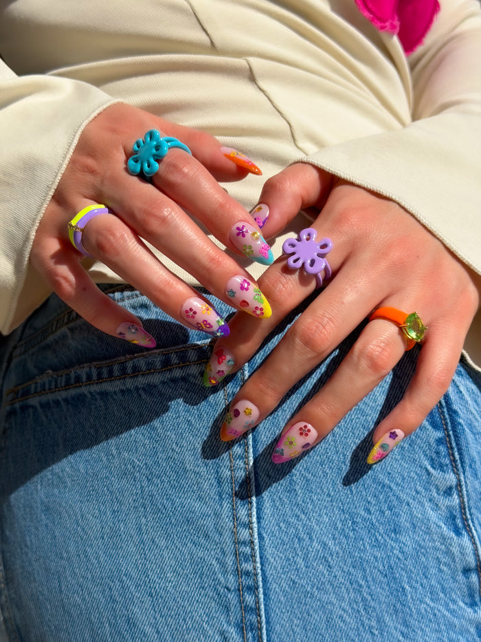 Hands with colorful floral and gem nails art stickers posed against denim.